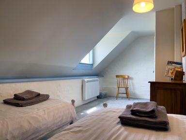 A bedroom with two beds and towels on each bed a wooden chair and a dresser with books at The Granary @ Canllefaes Penparc near Cardigan