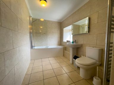 A bathroom with a bathtub shower sink toilet mirror and tiled walls and floor at The Granary @ Canllefaes in Penparc near Cardigan