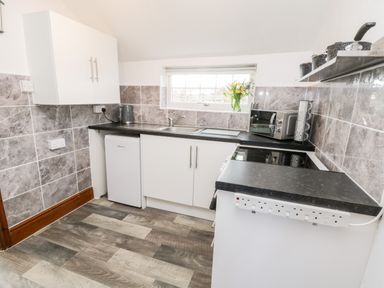 A kitchen with white cabinets a small refrigerator a microwave oven a kettle and a window with flowers on the sill at Hawthorn Dale Cottage Whitby