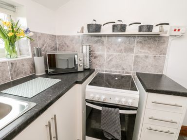 A kitchen countertop with a microwave knives in a block and flowers next to an electric stove with pots on a shelf above at Hawthorn Dale Cottage in Whitby