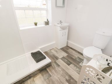 A bathroom with a toilet sink shower area and window with plant at Hawthorn Dale Cottage in Whitby
