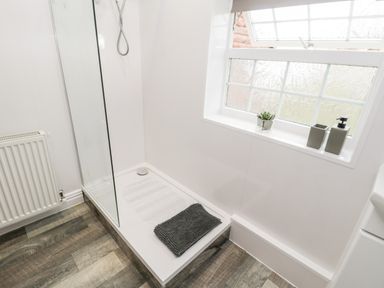 A bathroom shower area with a glass panel and a dark towel on the shower tray near a window with small plants and soap dispensers at Hawthorn Dale Cottage in Whitby