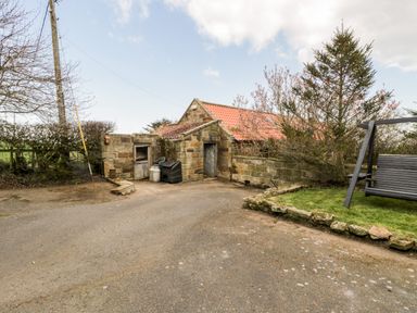 An outdoor area with a small stone building having two doors a grassy section with a swing and trees at Hawthorn Dale Cottage in Whitby