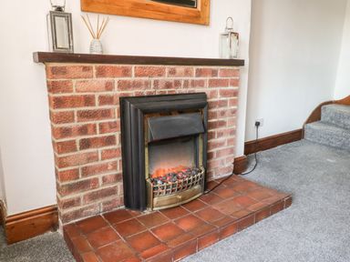 A fireplace with a brick surround and red tile hearth in a room with gray carpet at Hawthorn Dale Cottage Whitby