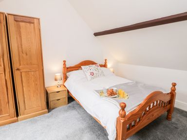 A bedroom with a wooden bed and wardrobe bedside tables with lamps and a tray with croissants and drinks on the bed at Hawthorn Dale Cottage in Whitby