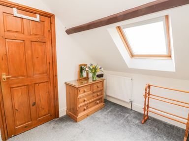 A room with a wooden door a wooden chest of drawers with a mirror and flowers a radiator a skylight window and a wooden towel rack at Hawthorn Dale Cottage in Whitby