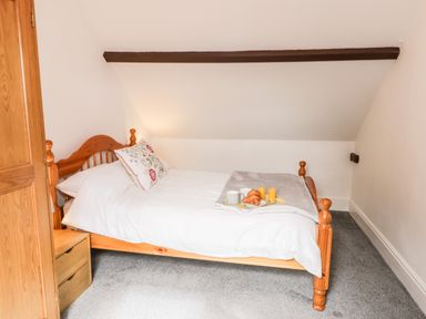 A bedroom with a wooden bed a side table and breakfast on the bed at Hawthorn Dale Cottage in Whitby
