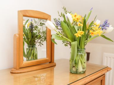A bouquet of flowers in a glass jar next to a wooden framed mirror on a wooden surface at Hawthorn Dale Cottage in Whitby