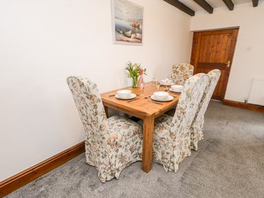 A dining room with a wooden table set for four and floral upholstered chairs at Hawthorn Dale Cottage in Whitby