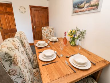 A dining table set with plates glasses cutlery and a vase of flowers in a room with wooden doors at Hawthorn Dale Cottage Whitby