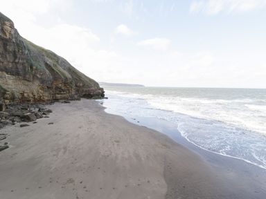 A sandy beach with waves and rocky cliffs on the side at Hawthorn Dale Cottage in Whitby