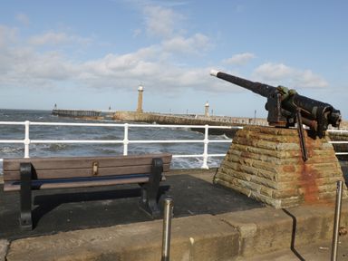 A bench and an old cannon on stone base overlooking a pier and lighthouse at Hawthorn Dale Cottage in Whitby
