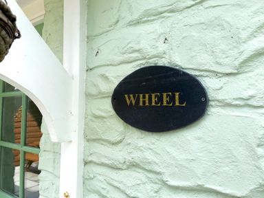 A black oval sign with gold letters saying Wheel on a pale green textured wall at The Wheel @ Canllefaes in Penparc near Cardigan