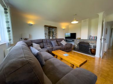 A living room with a large sectional sofa a wooden coffee table a fireplace and a mounted television at The Wheel @ Canllefaes in Penparc near Cardigan