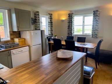 A kitchen with a wooden countertop island a dining table with chairs refrigerator dishwasher and windows with patterned curtains at The Wheel @ Canllefaes in Penparc near Cardigan