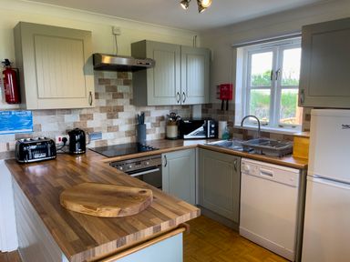 A kitchen with wooden countertops a sink a dishwasher a refrigerator a toaster a kettle and cabinets at The Wheel @ Canllefaes in Penparc near Cardigan