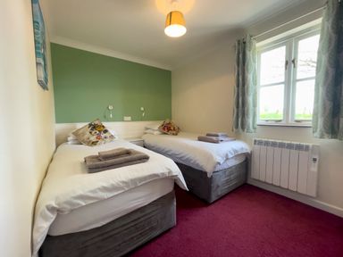 A bedroom with two single beds towels on beds window with curtains and wall lights at The Wheel @ Canllefaes in Penparc near Cardigan