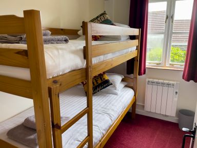 A bedroom with wooden bunk beds next to a window with red curtains at The Wheel @ Canllefaes in Penparc near Cardigan