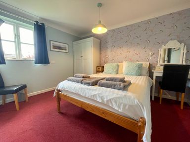 A bedroom with a wooden bed, two pillows, folded towels, a white wardrobe, a dressing table with a mirror, and a chair at The Wheel @ Canllefaes in Penparc near Cardigan