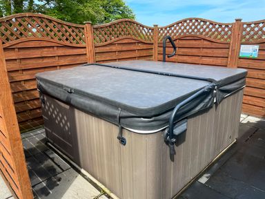 An outdoor hot tub with a cover and a wooden fence around it at The Wheel @ Canllefaes in Penparc near Cardigan
