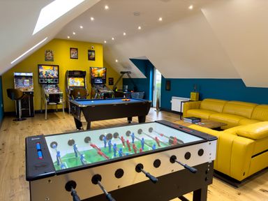 A game room with a foosball table pool table arcade machines and a yellow sofa at The Wheel @ Canllefaes in Penparc near Cardigan