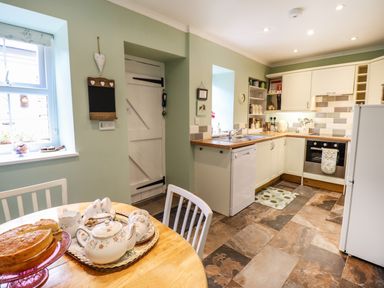 A kitchen with white cabinets a wooden table with tea set and cake at Coed Y Glyn in Llanuwchllyn near Bala