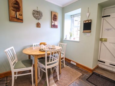 A dining area with a wooden table and four white chairs near a window and a door at Coed Y Glyn in Llanuwchllyn near Bala