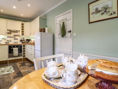 A kitchen with a table set with teacups and a cake on the table at Coed Y Glyn in Llanuwchllyn near Bala