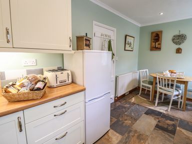 A kitchen with white cabinets a wooden countertop a toaster a white refrigerator a round wooden dining table with chairs and wall decorations at Coed Y Glyn in Llanuwchllyn near Bala