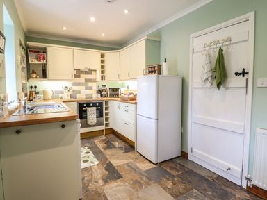 A kitchen with white cabinets a refrigerator a sink and utensils at Coed Y Glyn in Llanuwchllyn near Bala