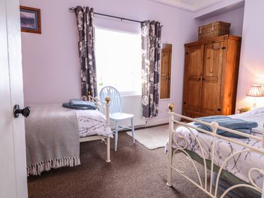 A bedroom with two single beds a wooden wardrobe a chair and a window with floral curtains at Coed Y Glyn in Llanuwchllyn near Bala