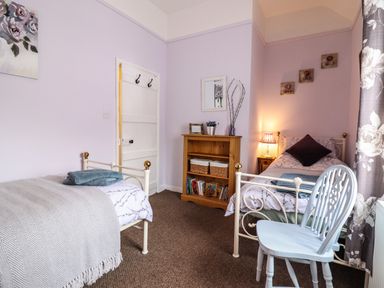 A bedroom with two single beds a wooden bookshelf a white chair and a lamp at Coed Y Glyn in Llanuwchllyn near Bala