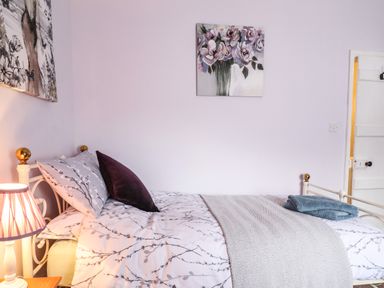 A bedroom with a single bed white metal frame with floral bedding and pillows a bedside lamp and two paintings on the wall at Coed Y Glyn in Llanuwchllyn near Bala