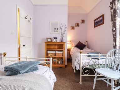 A bedroom with two single beds a wooden bookshelf a chair and curtains at Coed Y Glyn in Llanuwchllyn near Bala