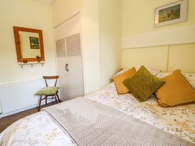 A bedroom with a bed with pillows and a blanket a wooden chair a mirror a shelf and a built in wardrobe at Coed Y Glyn in Llanuwchllyn near Bala