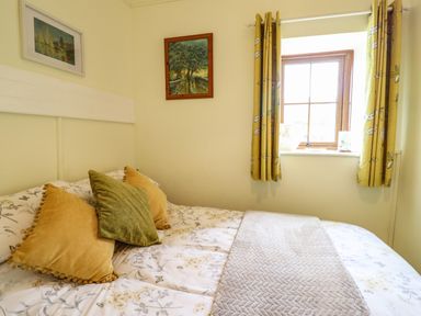 A bedroom with a bed with floral bedding and three pillows next to a window with yellow curtains at Coed Y Glyn in Llanuwchllyn near Bala