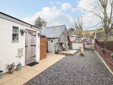 An outdoor area with two small buildings one labeled laundry and the other with a grey door two chairs along a stone wall and a wooden owl sculpture at Coed Y Glyn in Llanuwchllyn near Bala