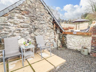 An outdoor patio area with two chairs and a table against a stone wall at Coed Y Glyn in Llanuwchllyn near Bala