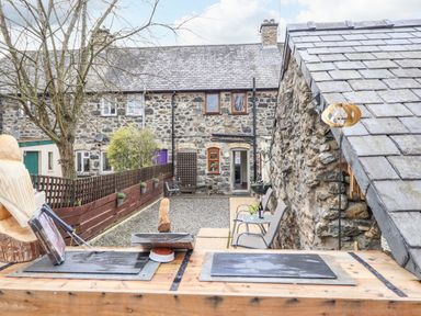 An outdoor patio area with gravel ground two chairs a small table with drinks and stone buildings at Coed Y Glyn in Llanuwchllyn near Bala
