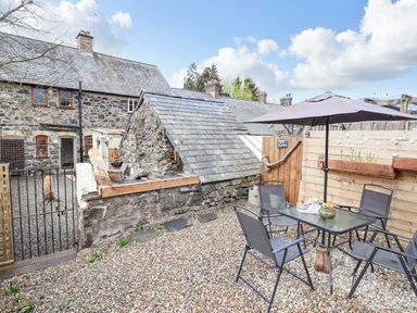 An outdoor patio area with a table, four chairs, and an umbrella next to a stone building at Coed Y Glyn in Llanuwchllyn near Bala