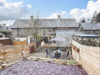 A backyard with a patio table and chairs under an umbrella surrounded by stone and wooden fences at Coed Y Glyn in Llanuwchllyn near Bala
