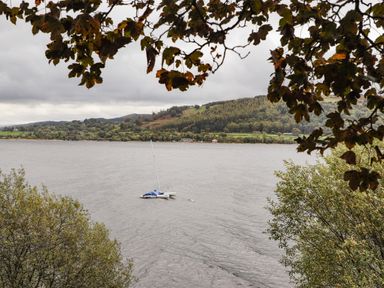 A lake with a small sailboat on the water surrounded by trees and hills at Coed Y Glyn Llanuwchllyn near Bala