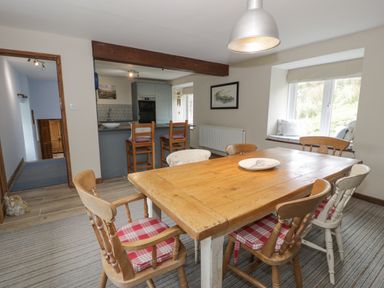 A dining room with a wooden table and chairs with red cushions next to a kitchen with bar stools at Pennant Tigi Uchaf in Dinas Mawddwy