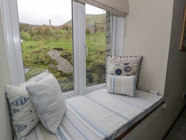 A window seat with cushions and a striped cushion cover overlooking a grassy landscape at Pennant Tigi Uchaf Dinas Mawddwy