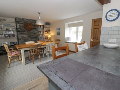 A dining room with wooden table and chairs stone wall bookshelf and a window seat at Pennant Tigi Uchaf in Dinas Mawddwy