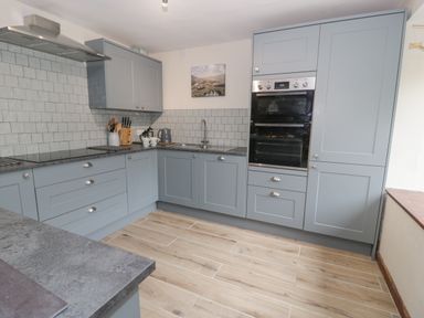A kitchen with grey cabinets built-in oven stove sink and wooden floor at Pennant Tigi Uchaf in Dinas Mawddwy
