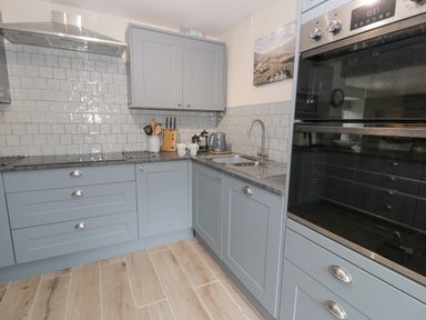 A kitchen with blue cabinets a countertop with utensils a kettle a double sink and a built in oven at Pennant Tigi Uchaf in Dinas Mawddwy