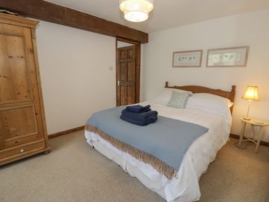 A bedroom with a double bed a wooden wardrobe a bedside table with a lamp and folded towels on the bed at Pennant Tigi Uchaf in Dinas Mawddwy