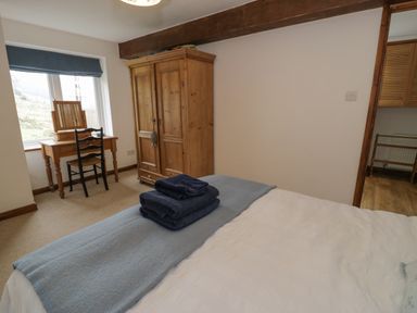 A bedroom with a bed with folded towels a wooden wardrobe a wooden dressing table and chair at Pennant Tigi Uchaf in Dinas Mawddwy