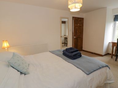 A bedroom with a bed made with white linens and blue towels on top a wooden door a lamp and a window at Pennant Tigi Uchaf in Dinas Mawddwy